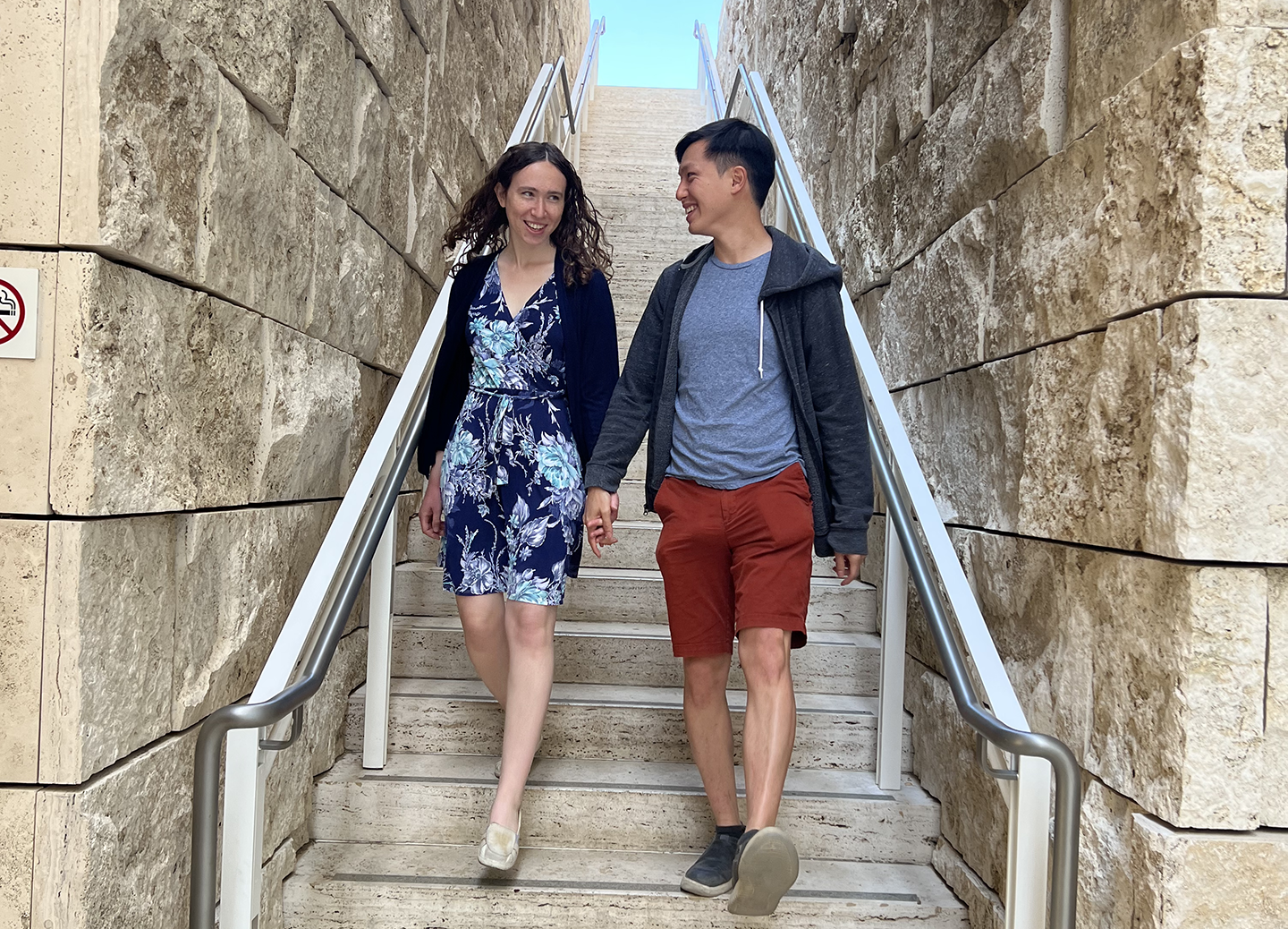 Sam and Zhi walking down an outdoor staircase made of stone, holding hands and smiling